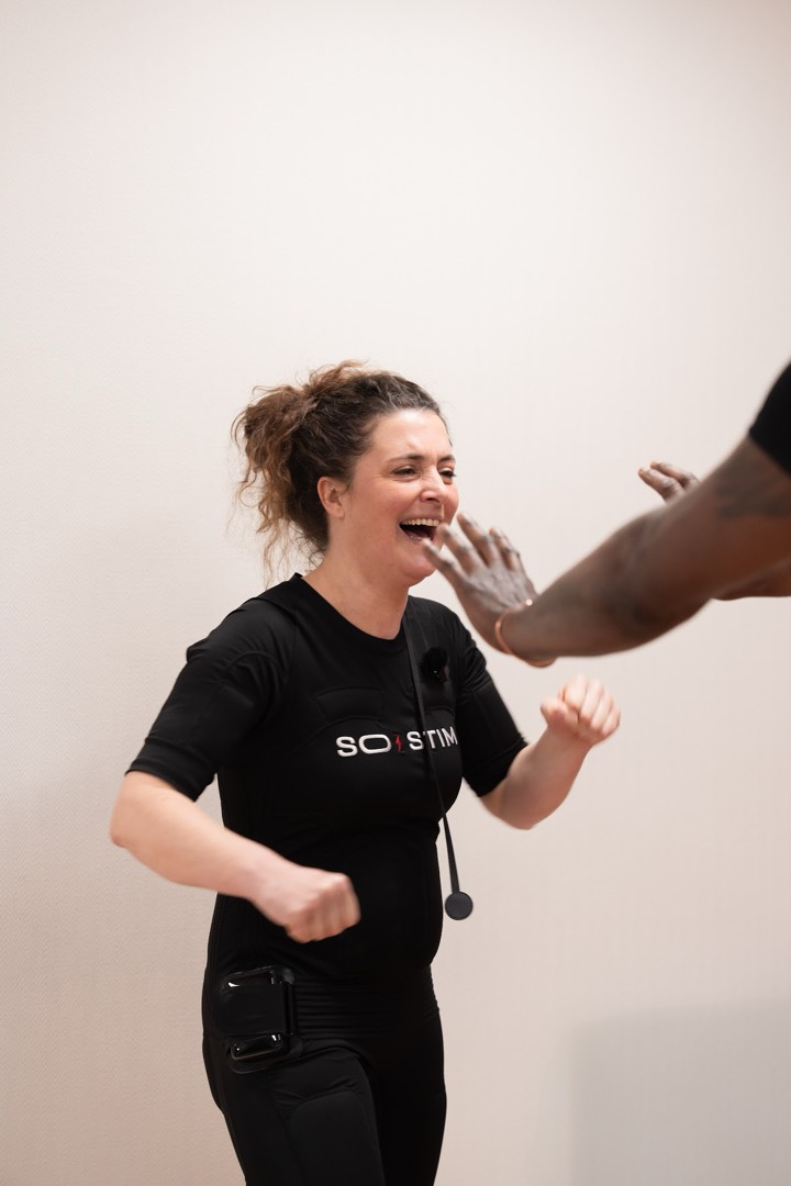 Femme motivée en combinaison EMS, poings serrés, accompagnée par son coach EMS
