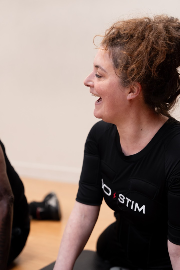 Femme souriante en combinaison EMS pendant une séance d'électrostimulation en studio SO STIM