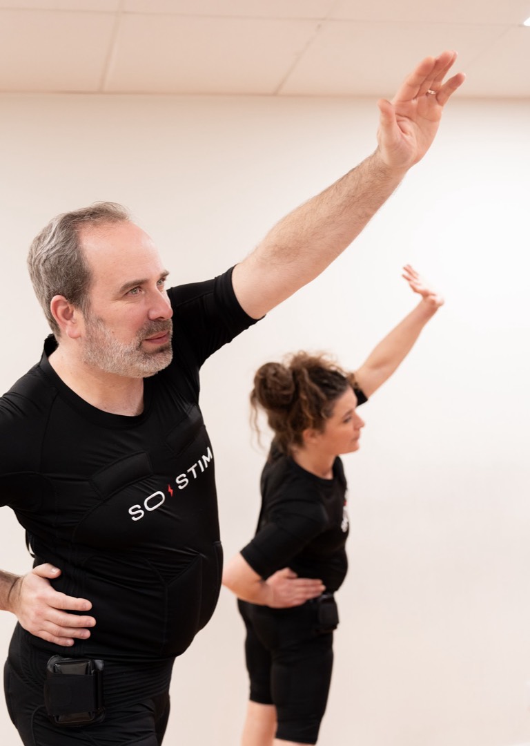 Pratiquants en combinaison EMS bras levés dans un studio lumineux, performance sportive