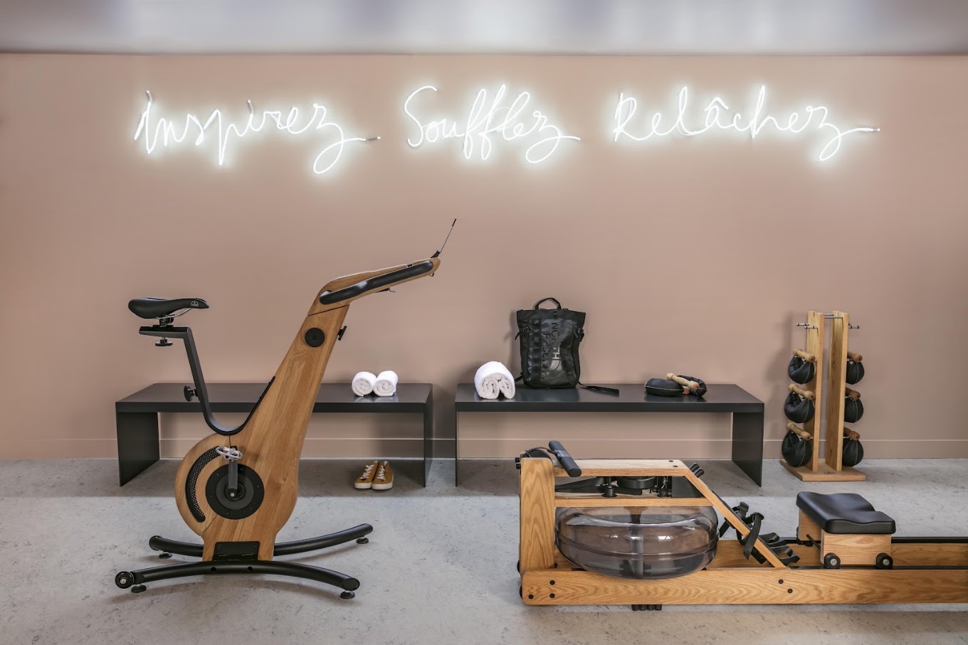 Studio SO STIM Paris 10e à l'OKKO Hotels Gare de l'Est : vélo et rameur en bois sous le néon « Inspirez, Soufflez, Relâchez »